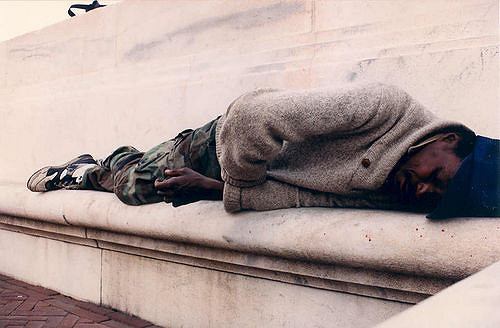 A homeless man sleeps in front of a building. 