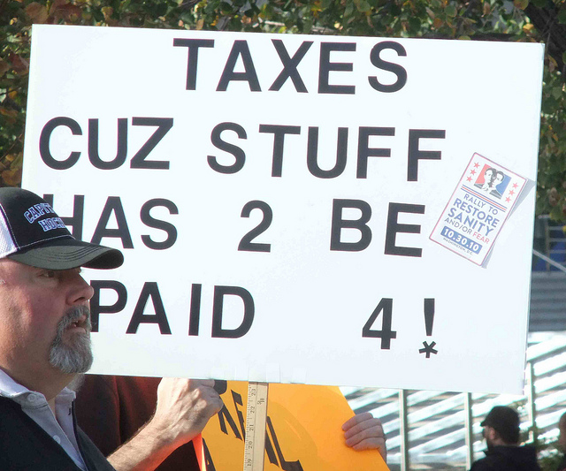 Protest sign reading "TAXES CUZ STUFF HAS 2 BE PAID 4"