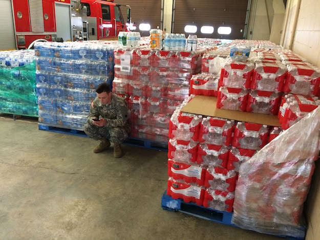 U.S. Army service member crouching next to pallets of water bottles in Flint, Mich.