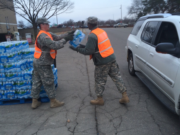 National Guard service members hand off cases of plastic water bottles into cars as they drive up