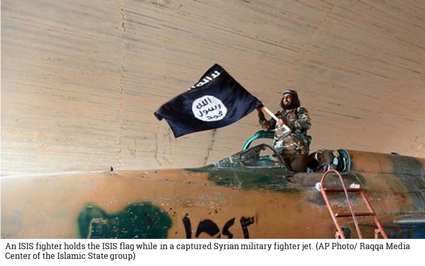 An ISIS fighter holds the ISIS flag while standing in a captured Syrian military fighter jet. (AP Photo/ Raqqa Media Center of the Islamic State group)