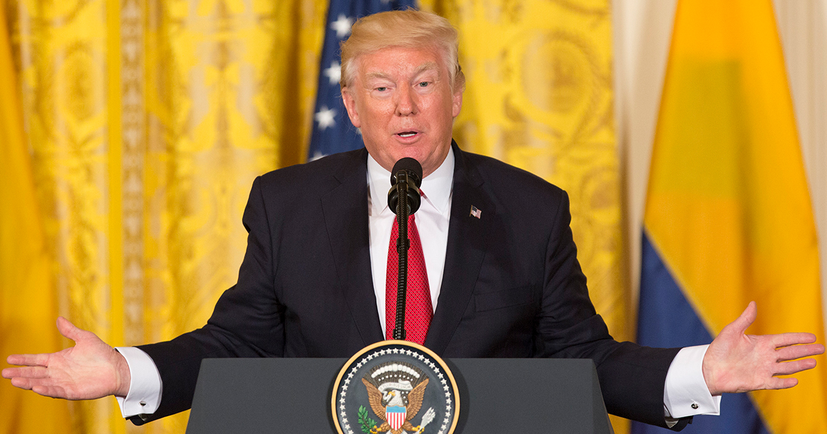 trump-standing-at-podium-arms-wide-yellow-background